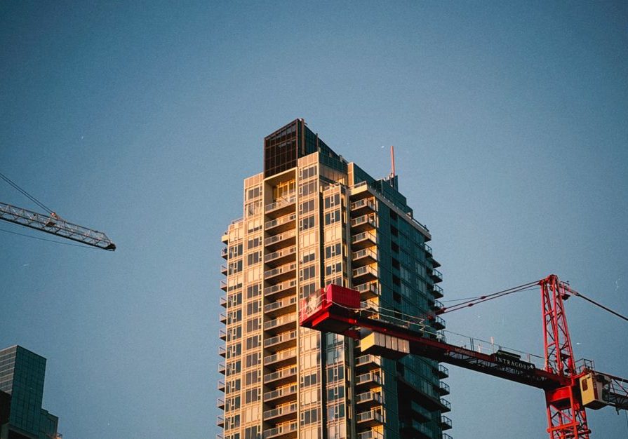 High-rise building with cranes in urban area against blue sky backdrop.