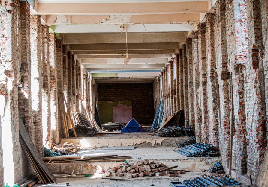 An empty industrial interior undergoing renovation, with exposed brick and construction materials.